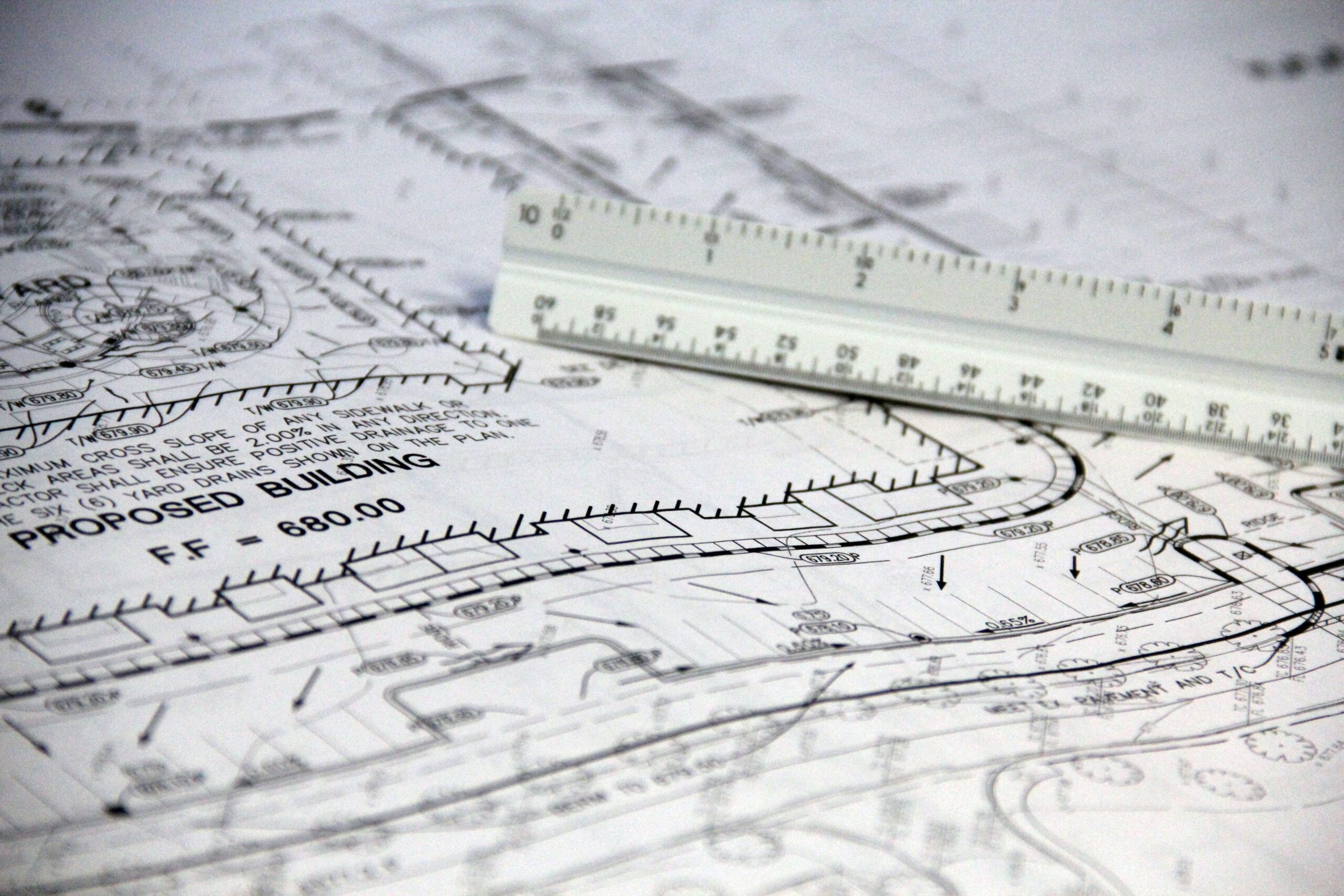 Services Detailed close-up of architectural blueprints with scale ruler, showing building plans and measurements.