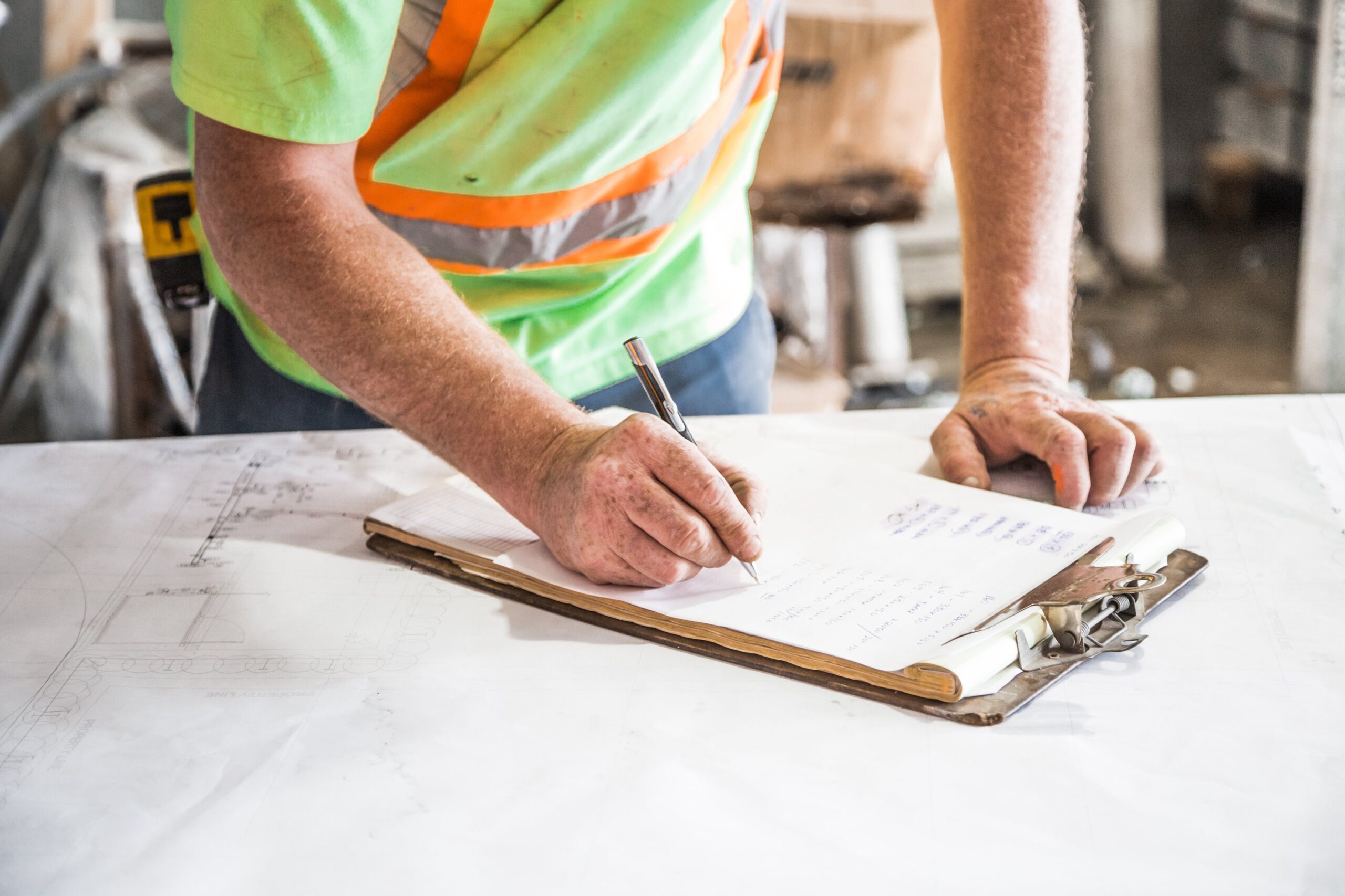Services A construction worker writes notes on a clipboard at a construction site, emphasizing planning and precision.