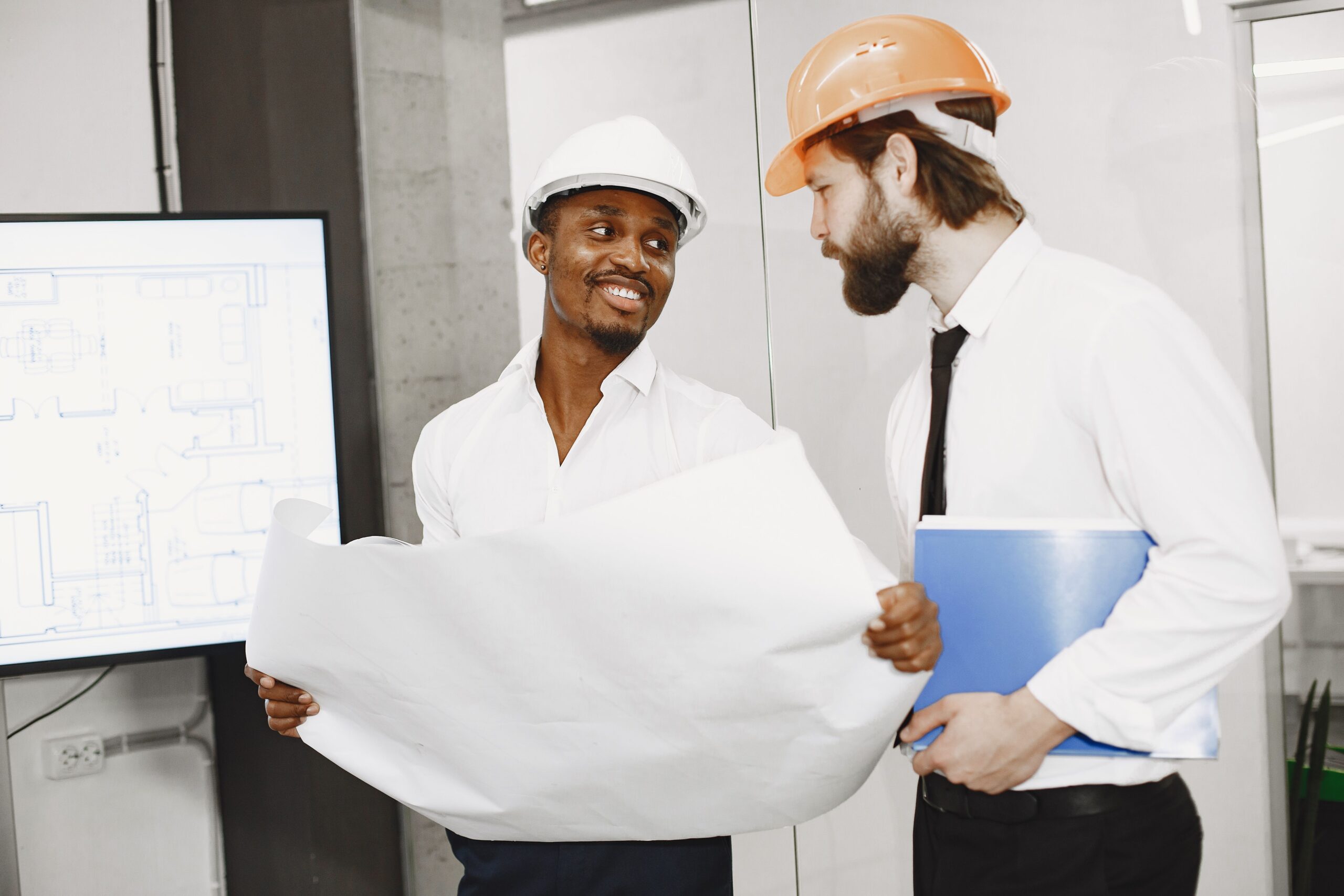 Services Two architects in hard hats discuss blueprints in a modern office setting, highlighting teamwork and planning.
