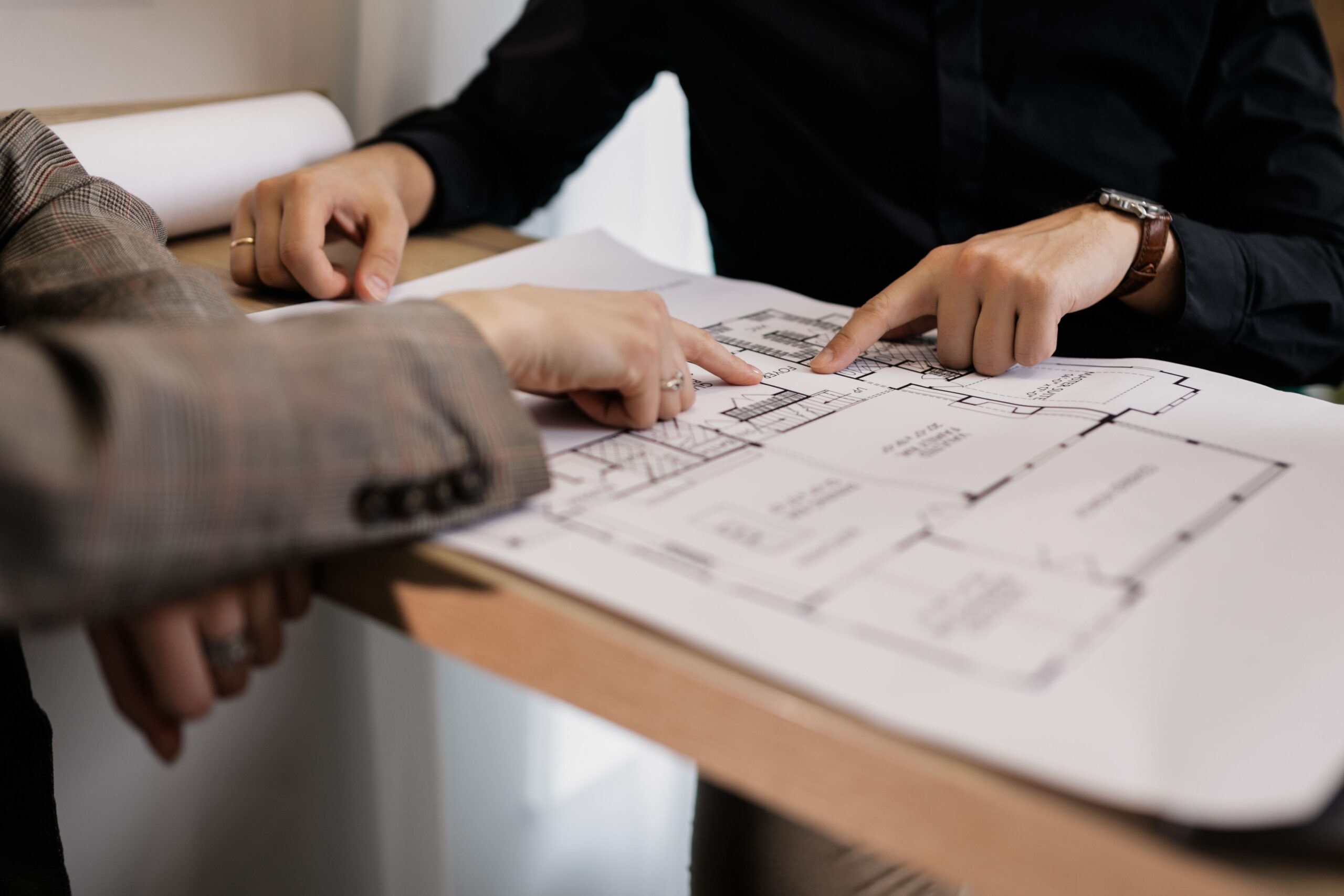 Services Two architects reviewing and pointing at a detailed floor plan on paper in an office setting.